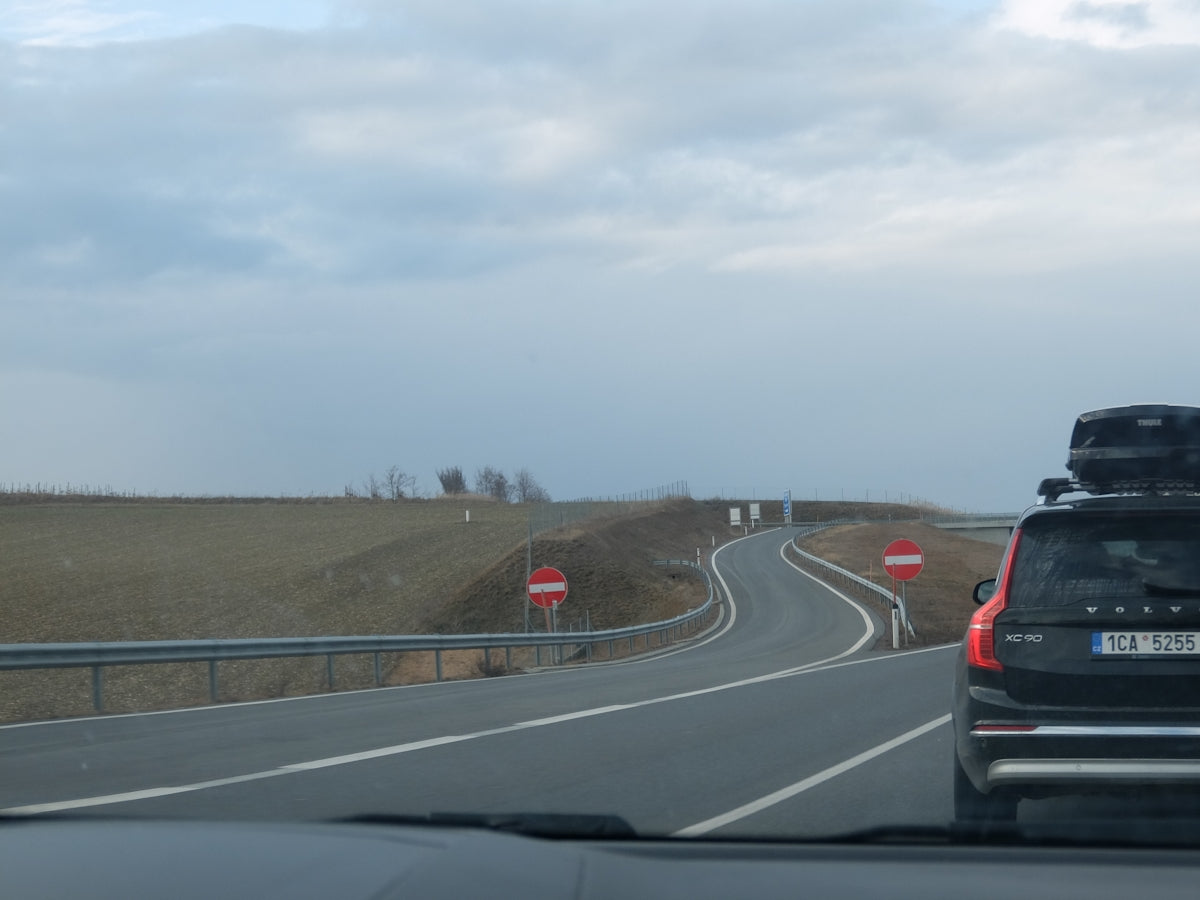 A car drives on a quiet highway under a cloudy sky.