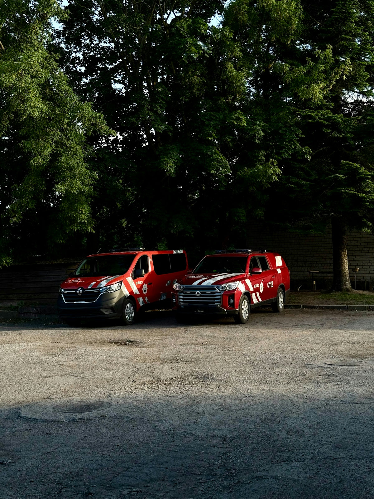 Red emergency vehicles parked near some trees.