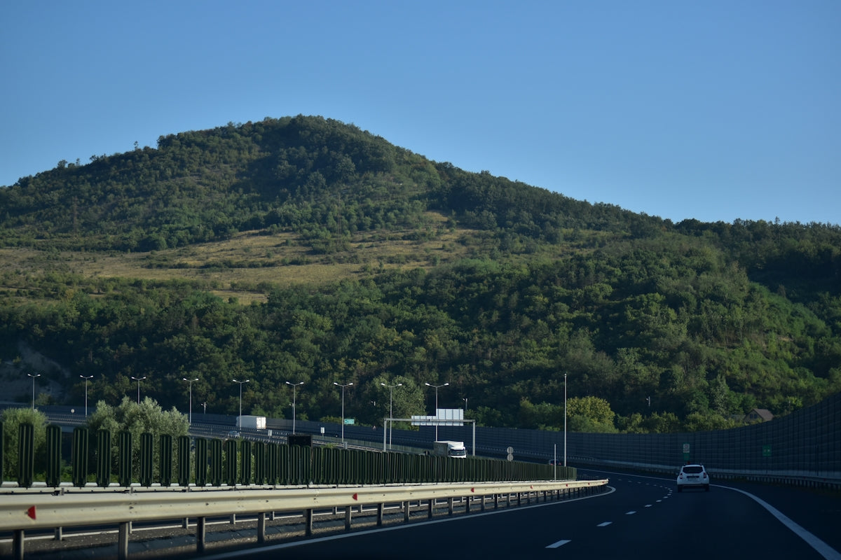 Highway passing by a lush green forested hill under clear sky.
