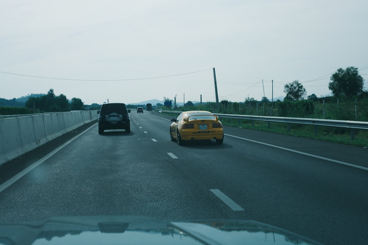 Two cars driving on a highway under cloudy sky.