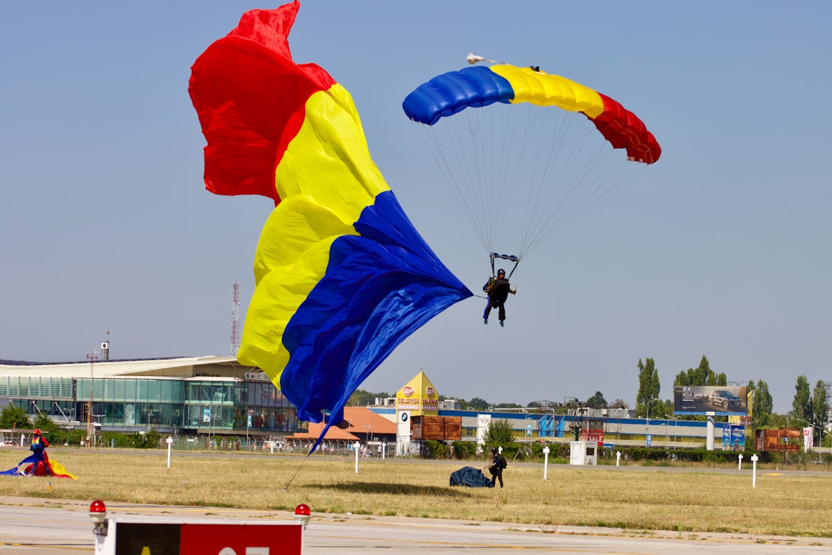 Parachutists descend near a romanian flag.