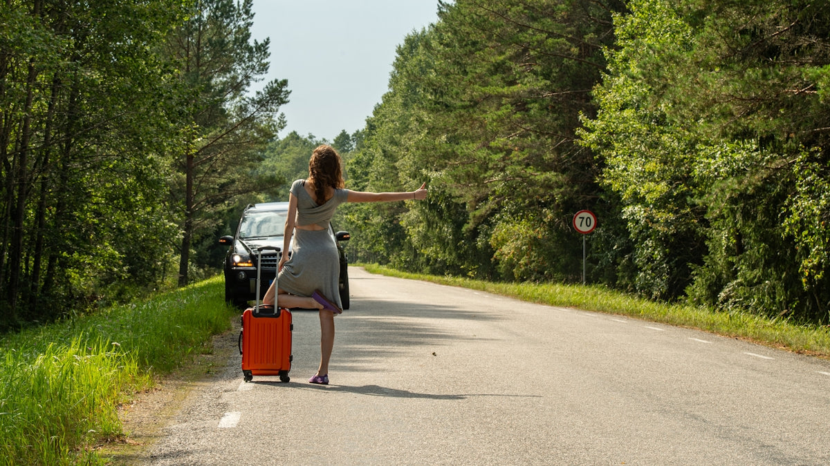 Woman hitchhiking with suitcase on roadside