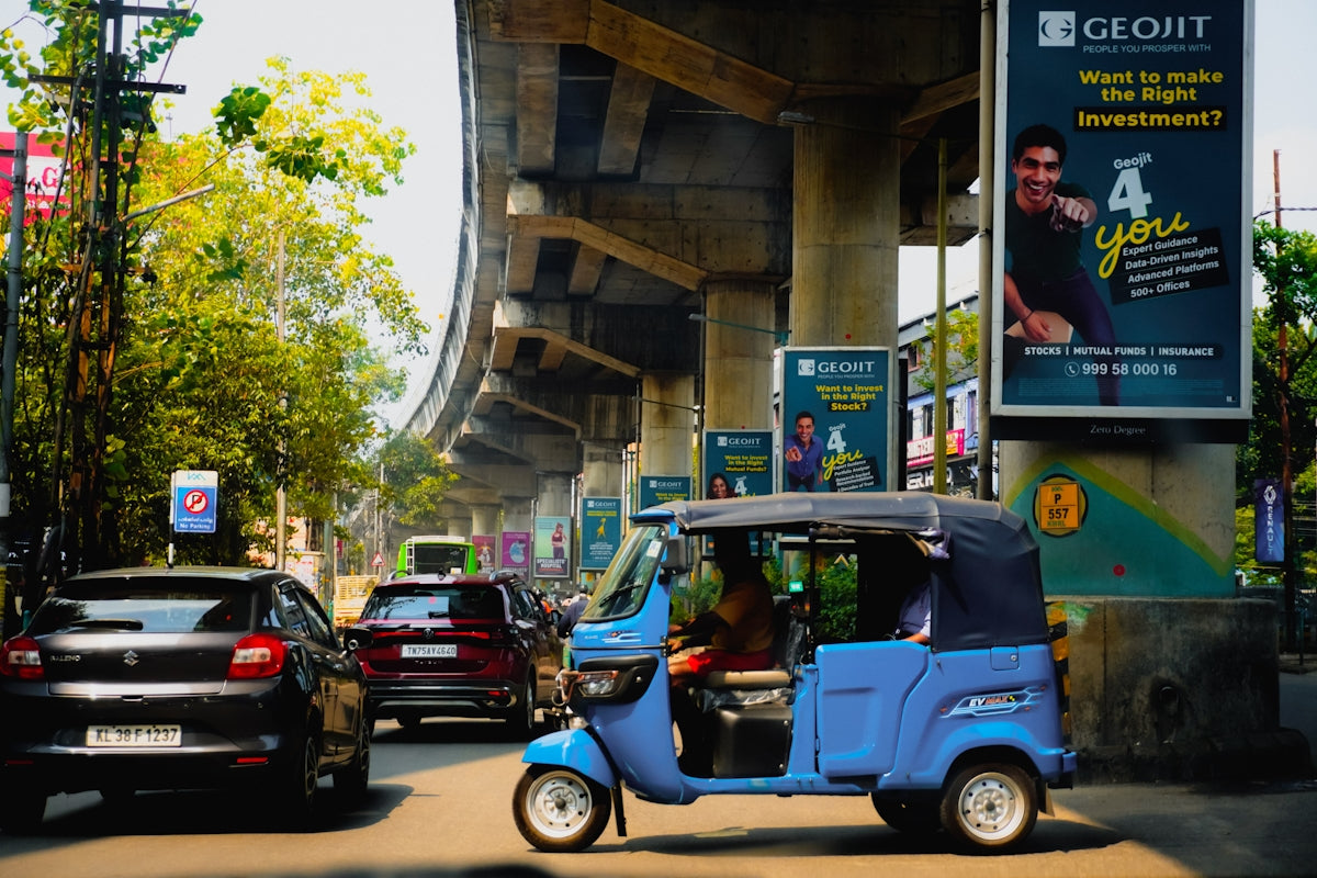 A blue auto-rickshaw drives on a busy street.