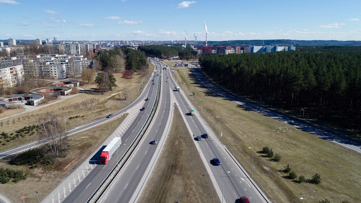 Cars and truck on a highway with cityscape and forest.