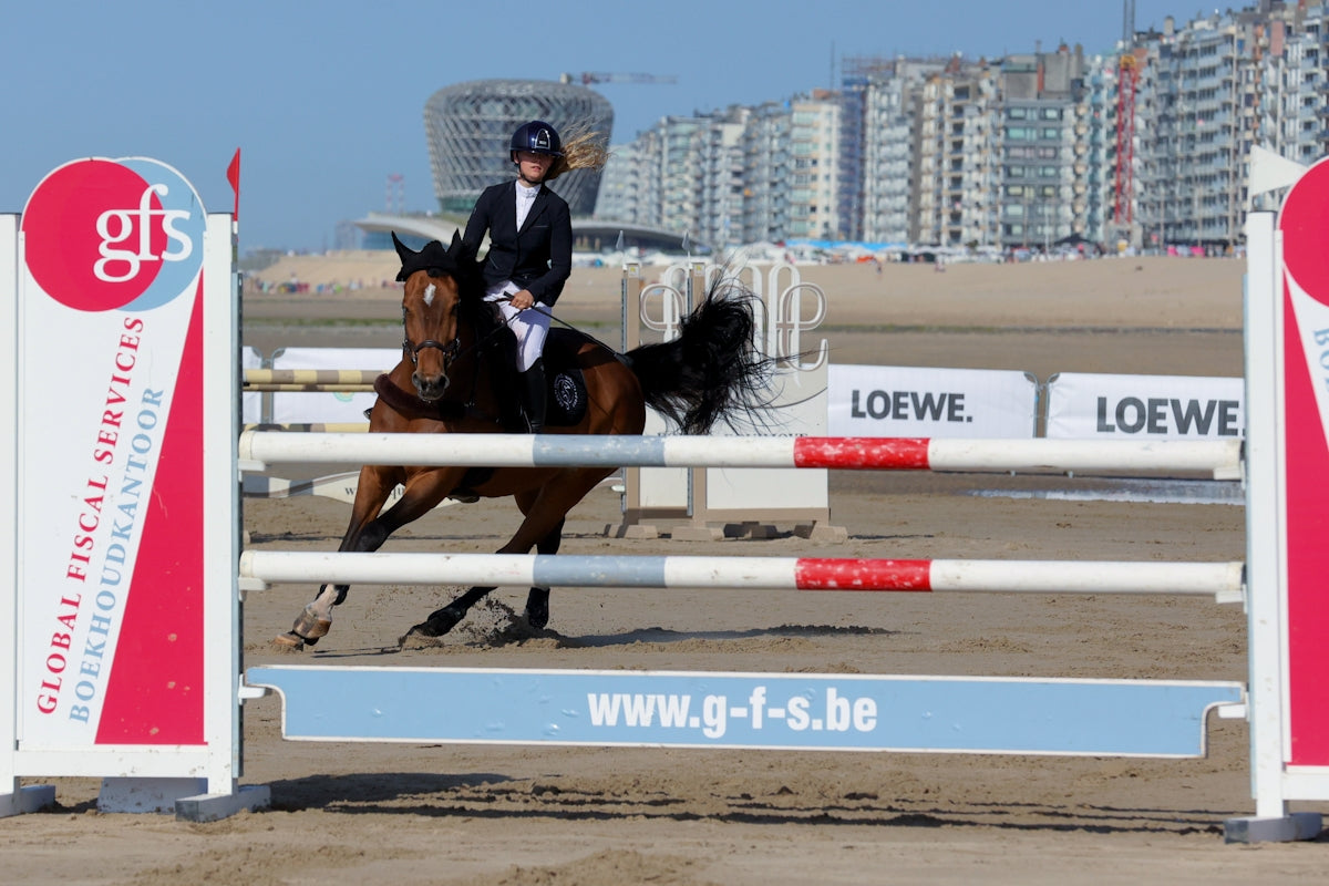 Equestrian horse and rider jumping over an obstacle on sand.