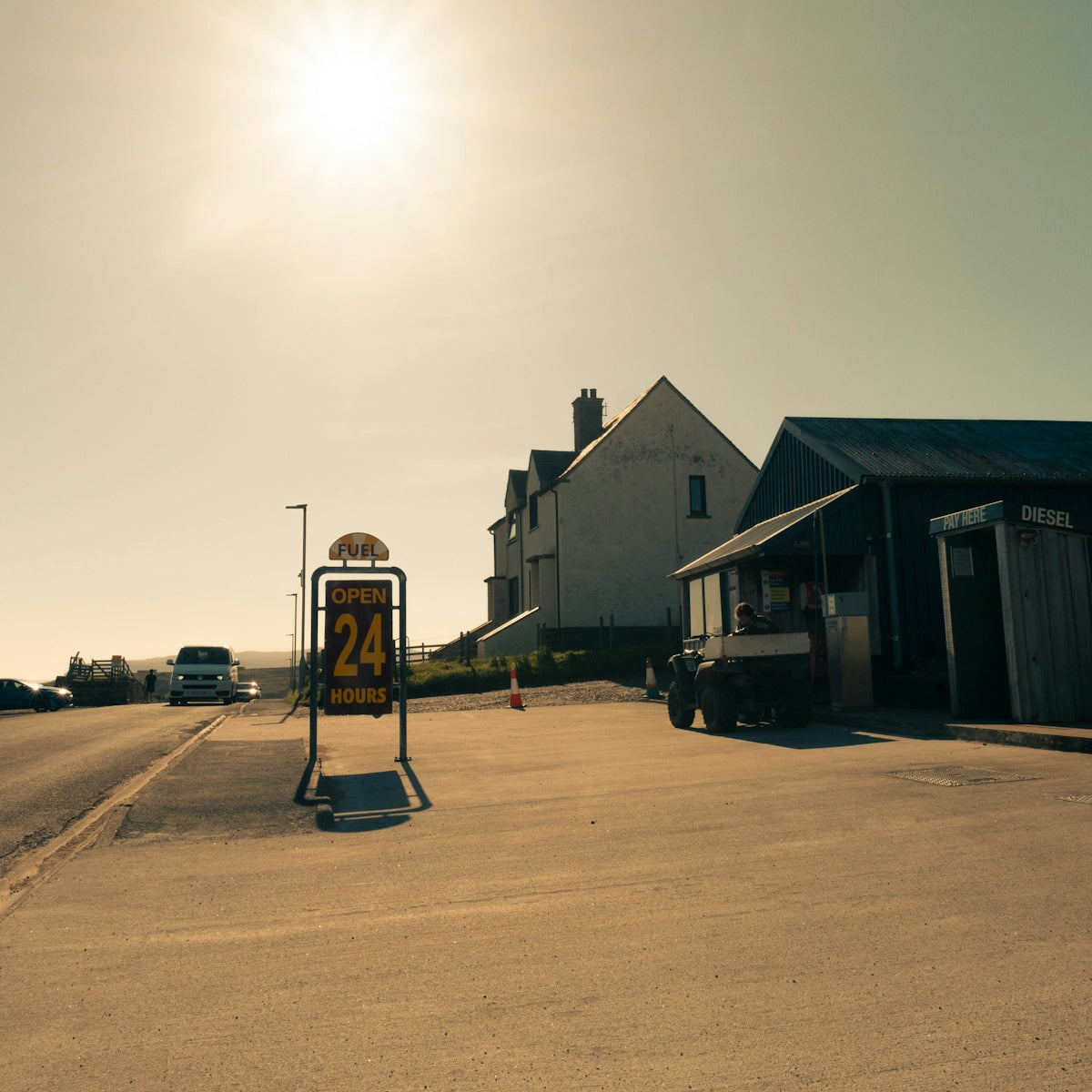 Roadside 'open 24 hours' sign under bright, sunny sky.