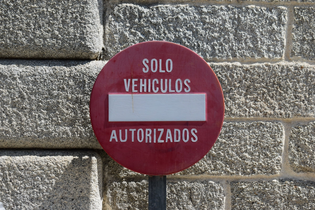 Red circular sign solo vehiculos autorizados on a stone wall.