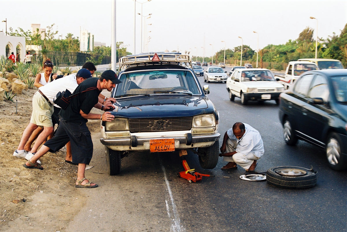 Men push a car while another changes its flat tire.