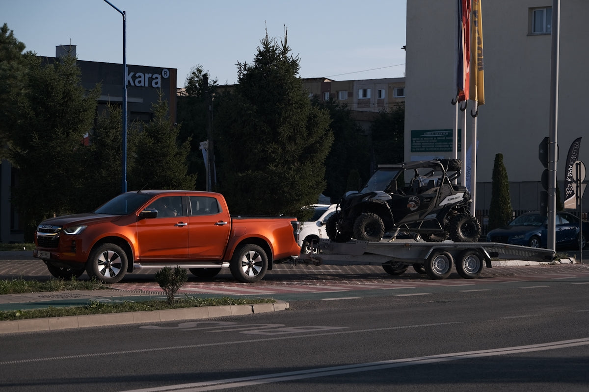 An orange pickup truck towing a black off-road vehicle on a trailer.